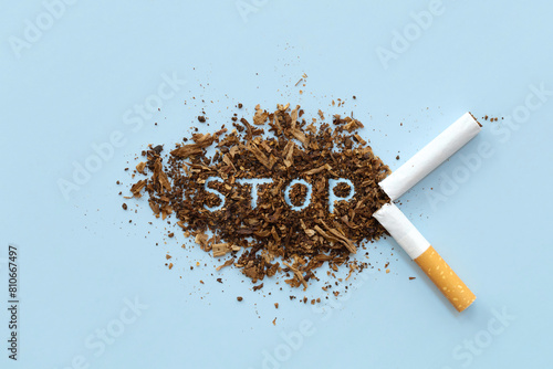 Fotografie Broken cigarette scattered tobacco with text STOP on a light blue background