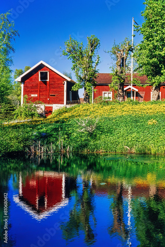 Red cottages by a lake with reflections in the water in summer © Lars Johansson