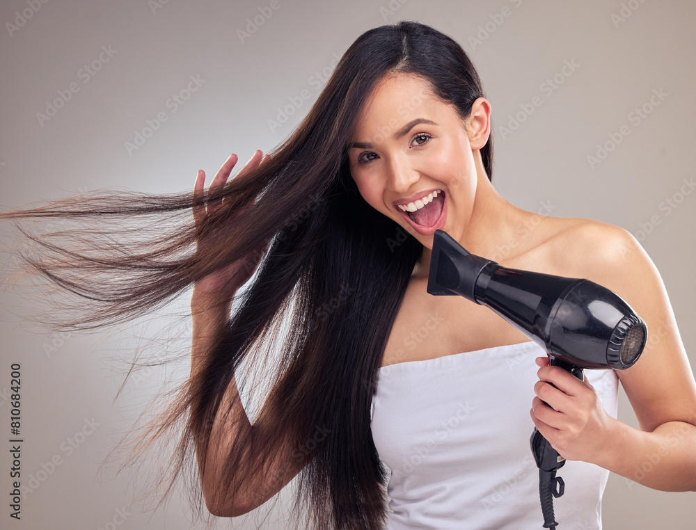 Asian woman, hairdryer and happy with portrait in studio for growth, straighten and brazilian treatment on gray background. Female person, excited and proud with clean hair, keratin and hairstyle Asian woman, hairdryer and happy with portrait in studio for growth, straighten and brazilian treatment on gray background. Female person, excited and proud with clean hair, keratin and hairstyle
