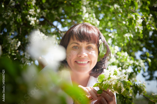Girl walking and Relaxing near Blossoming apple Tree on Sunny Day. Portrait of Middle aged woman enjoying nature surrounded by white blossoms