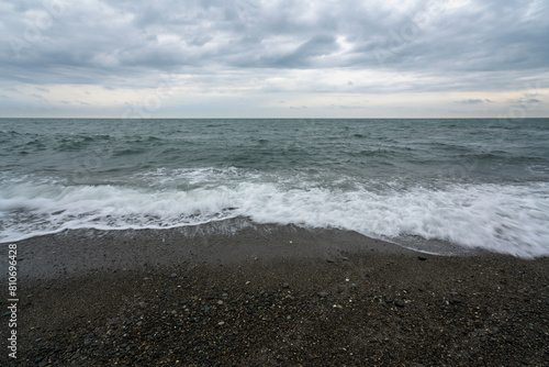 An incoming wave on the Black Sea and a pebble beach on the Sochi coast on a summer day with clouds, Sochi, Krasnodar Territory, Russia
