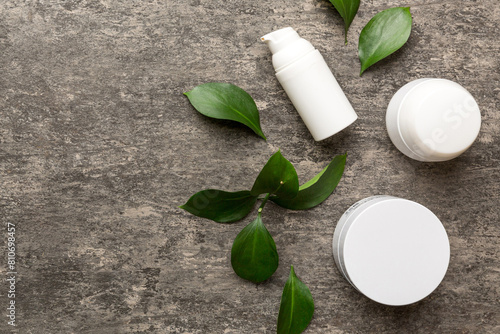Organic cosmetic products with green leaves on cement background. Copy space, flat lay