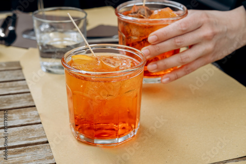 a woman's hand holds a glass of aperol spritz with ice and Prosecco, a traditional Italian aperitif. 