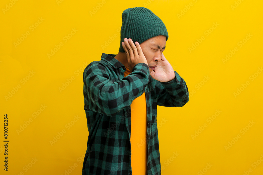 Side view of Annoyed young Asian man covers his ears and appears to be screaming or shouting, experiencing a painful earache possibly due to otitis exacerbated by loud noise Side view of Annoyed young Asian man covers his ears and appears to be screaming or shouting, experiencing a painful earache possibly due to otitis exacerbated by loud noise