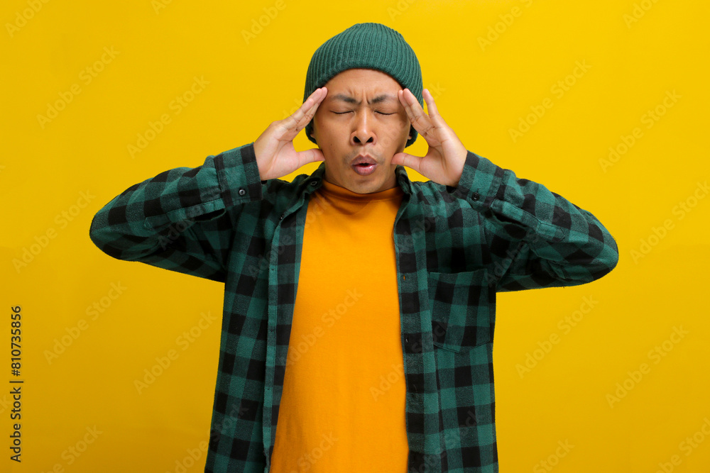 Nervous young Asian man is taking steps to calm down, focusing on breathing techniques, possibly relieving a headache or managing stress, isolated on a yellow background Nervous young Asian man is taking steps to calm down, focusing on breathing techniques, possibly relieving a headache or managing stress, isolated on a yellow background