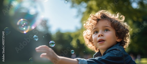 A young boy blows soap bubbles in a park as captured in a portrait with copy space image