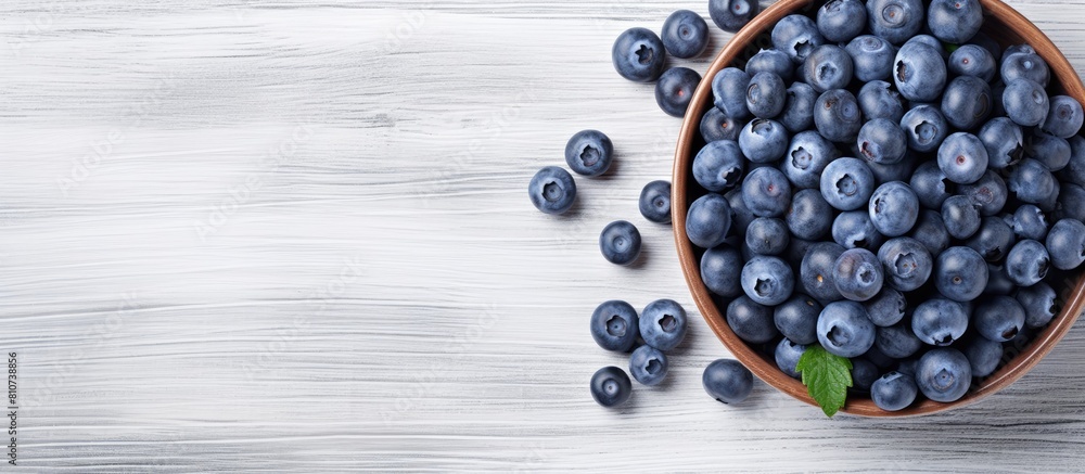 A summery image of ripe blueberries arranged in a blue bowl on a white wooden surface seen from above The flat overhead perspective leaves plenty of empty space for text or other elements A summery image of ripe blueberries arranged in a blue bowl on a white wooden surface seen from above The flat overhead perspective leaves plenty of empty space for text or other elements