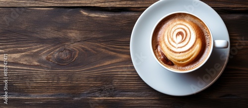 A top down view of a cup of coffee or cappuccino alongside a plate of traditional Swedish cinnamon buns known as kanelbulle The image is set against a wooden background offering ample copy space photo