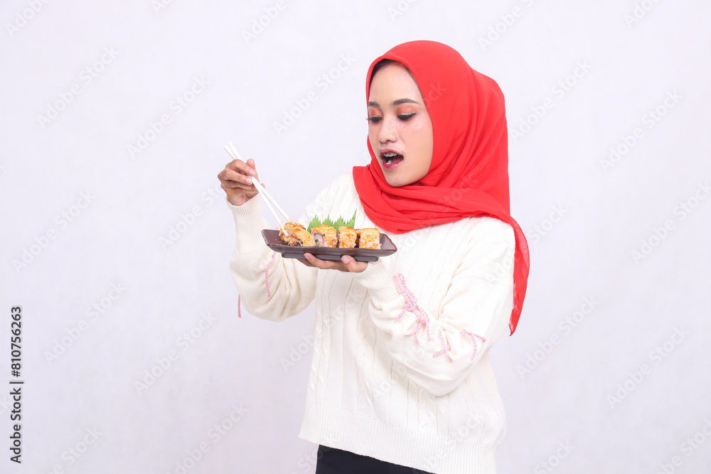 indonesia woman in hijab surprised at sushi holding chopsticks and bringing it to a plate containing sushi (Japanese food). Beautiful Muslim women are used for culinary, food and advertising content indonesia woman in hijab surprised at sushi holding chopsticks and bringing it to a plate containing sushi (Japanese food). Beautiful Muslim women are used for culinary, food and advertising content
