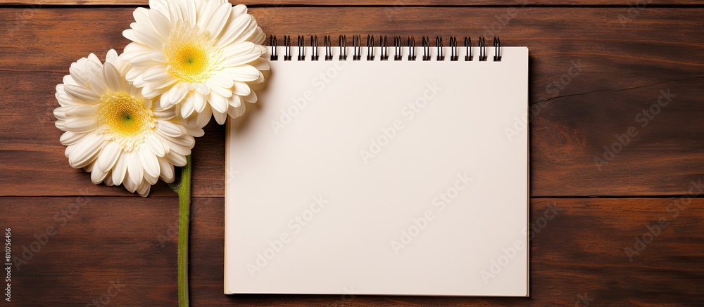 Top view copy space image of three gerbera flowers and a blank paged notebook resting on a wooden table Top view copy space image of three gerbera flowers and a blank paged notebook resting on a wooden table