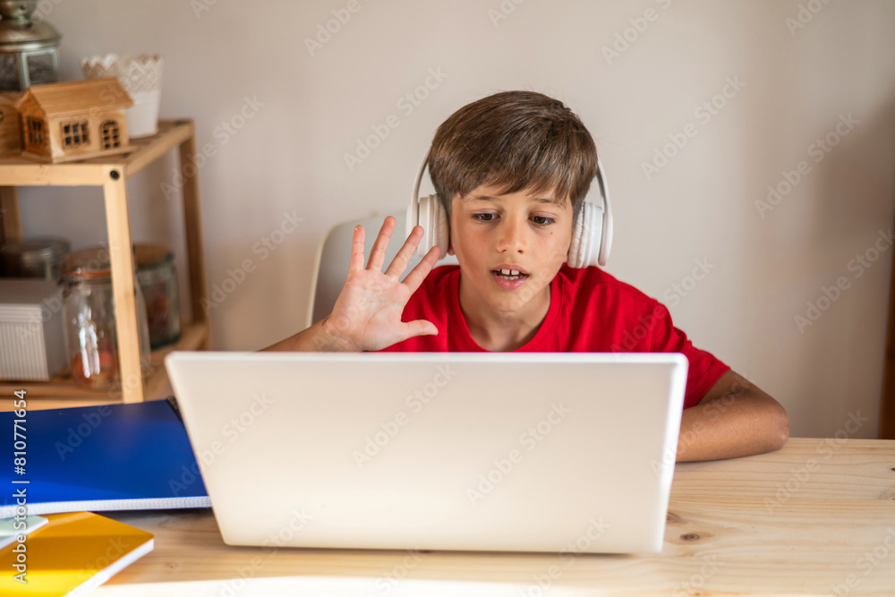 Elementary Boy Participating in a Distance Class Using a Laptop and Headphones for His Virtual Class. Student Talking to the Teacher Through Video Calls to Resolve Doubts About the School Topic. Elementary Boy Participating in a Distance Class Using a Laptop and Headphones for His Virtual Class. Student Talking to the Teacher Through Video Calls to Resolve Doubts About the School Topic.