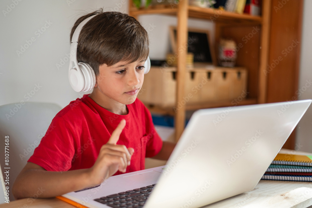 Homeschool Boy Participating in a Distance Class Using a Laptop and Headphones for His Virtual Class. Student Talking With the Teacher Through Video Calls to Resolve Doubts About the School Topic. Homeschool Boy Participating in a Distance Class Using a Laptop and Headphones for His Virtual Class. Student Talking With the Teacher Through Video Calls to Resolve Doubts About the School Topic.
