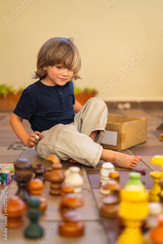 Adorable 4 Year Old Blonde Boy Playing With Colorful Wooden Pieces In The Yard Of His House.