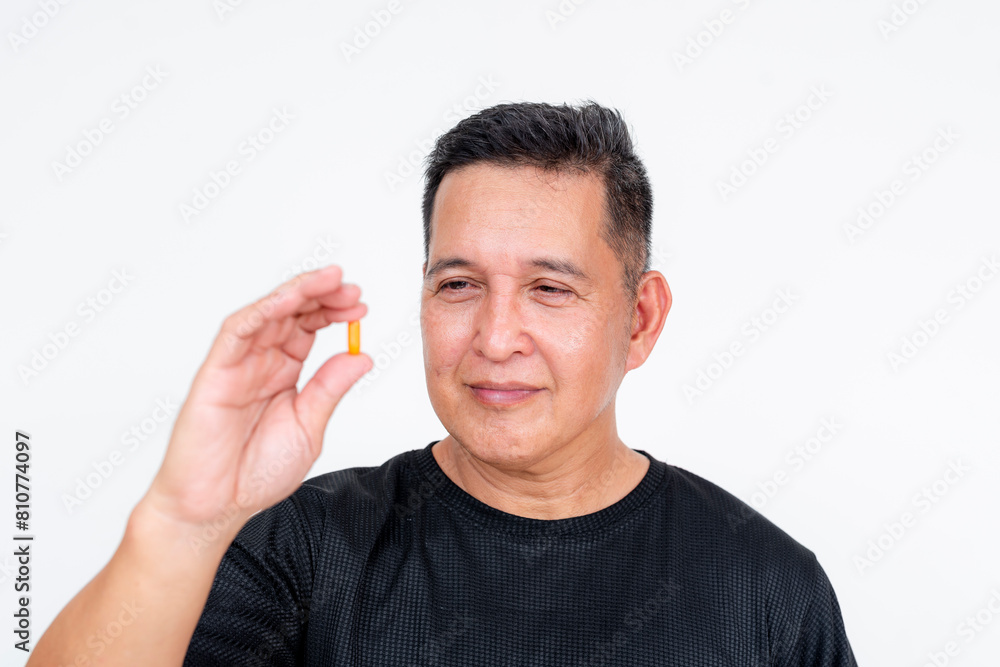 A middle-aged Asian man holds a multivitamin capsule, displaying it prominently against a white background, focusing on health and wellness. A middle-aged Asian man holds a multivitamin capsule, displaying it prominently against a white background, focusing on health and wellness.