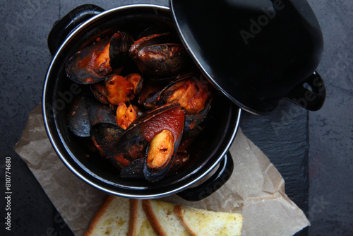 A dish of mussels. Fresh mussels in a black saucepan in tomato sauce. A traditional seafood dish. White bread crackers. Top view. Copy space.