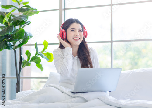 Asian beautiful woman girl in her bedroom smiling relaxed searching, playing social on her laptop with headphones listening to music on white bed in the morning after waking up at home. Free Download Asian beautiful woman girl in her bedroom smiling relaxed searching, playing social on her laptop with headphones listening to music on white bed in the morning after waking up at home. - GFXLoad