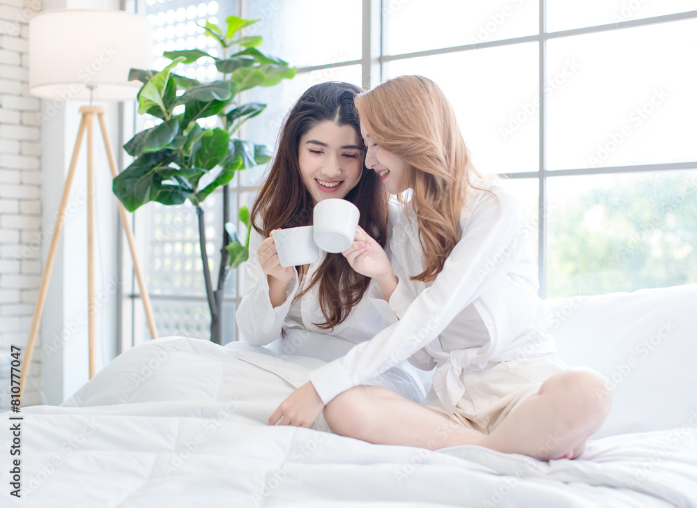Two beautiful Asian female girls drinking coffee in a bedroom, Cheerful young woman smiling, happy sitting on the bed, having a conversation, drinking tea, weekend breakfast lifestyle at home Two beautiful Asian female girls drinking coffee in a bedroom, Cheerful young woman smiling, happy sitting on the bed, having a conversation, drinking tea, weekend breakfast lifestyle at home