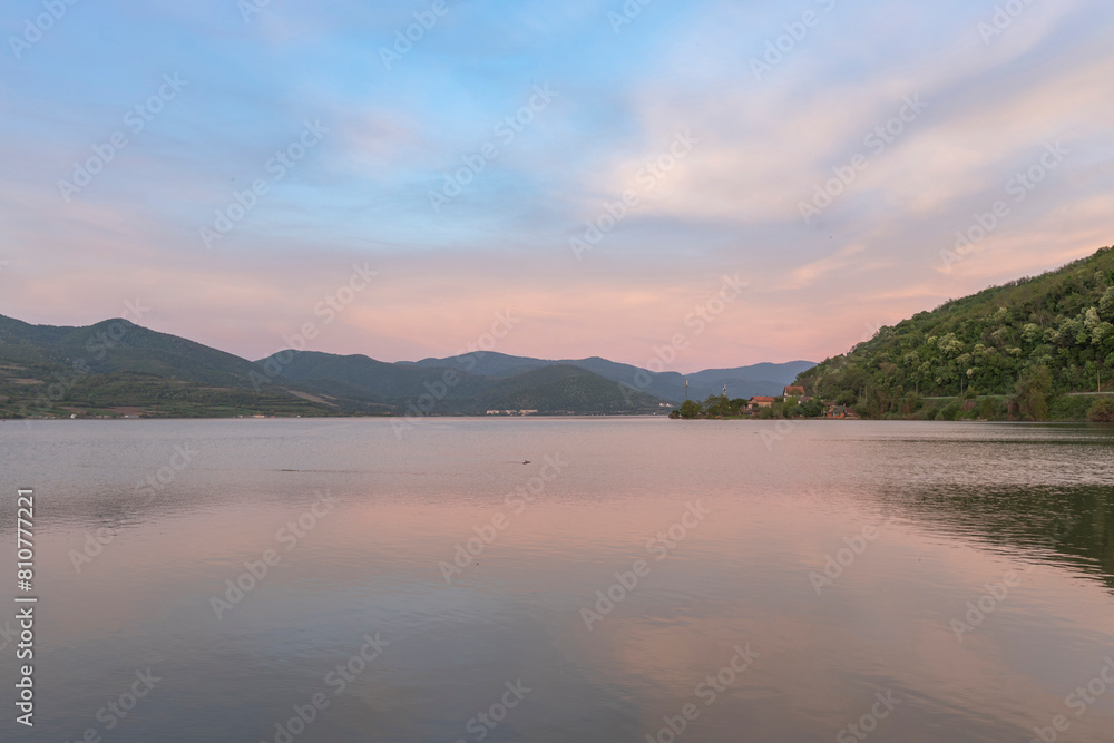 A serene sunset over a tranquil lake with rippled water, mountains in the distance, and a clear sky with soft clouds A serene sunset over a tranquil lake with rippled water, mountains in the distance, and a clear sky with soft clouds