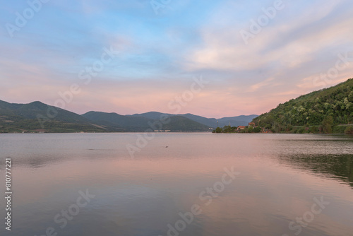  A serene sunset over a tranquil lake with rippled water  mountains in the distance  and a clear sky with soft clouds