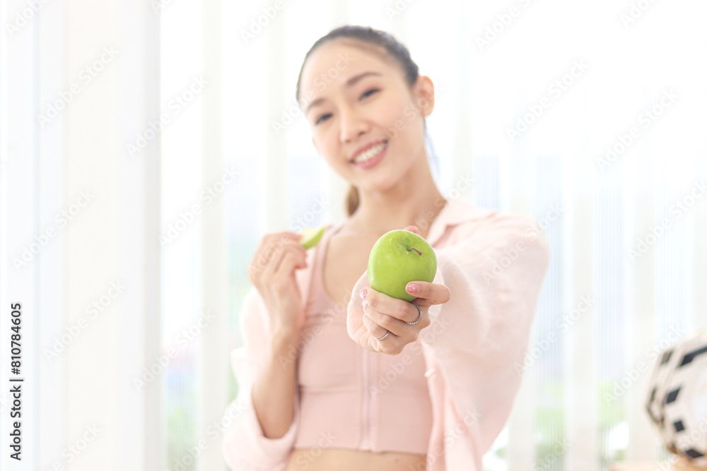 Sporty girl in fitness sport wear giving green apple to camera. Beautiful happy Asian woman in kitchen eats fruit for healthy. Losing weight and getting slim, healthy food fitness workout Sporty girl in fitness sport wear giving green apple to camera. Beautiful happy Asian woman in kitchen eats fruit for healthy. Losing weight and getting slim, healthy food fitness workout