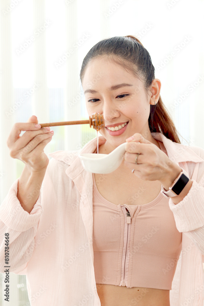 Beautiful happy smiling Asian woman looking at good honey source of sweetness for healthy food and beverage drink. Sporty girl making healthy diet from sweet honey to lose weight, get slim and healthy Beautiful happy smiling Asian woman looking at good honey source of sweetness for healthy food and beverage drink. Sporty girl making healthy diet from sweet honey to lose weight, get slim and healthy