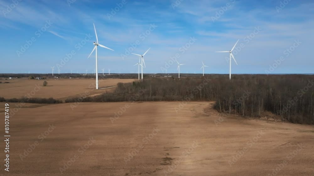 Wind turbines spin in a sunny field, framed by blue skies and a line of trees, capturing a serene energy scene Wind turbines spin in a sunny field, framed by blue skies and a line of trees, capturing a serene energy scene