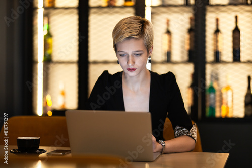 A professional young woman concentrates on her work on a laptop in a cozy café environment, displaying focus and determination.