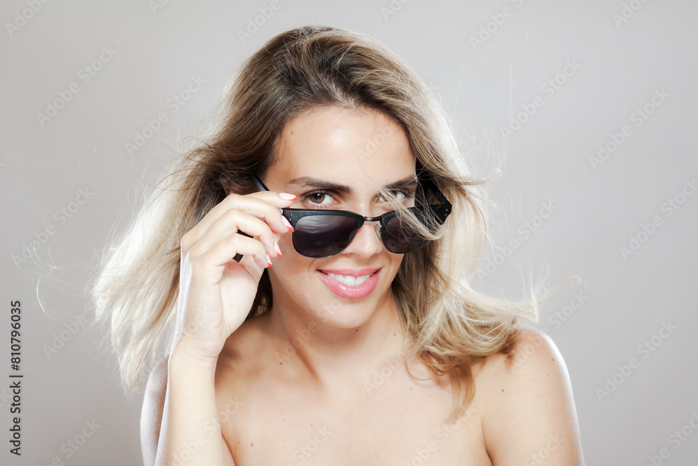 Stylish woman playfully lifting her sunglasses with a confident smile Stylish woman playfully lifting her sunglasses with a confident smile