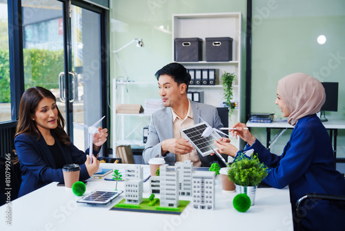 Trio of businesspeople, including a middle-aged Asian man and woman, strategize at their desk, prioritizing sustainability renewable energy adoption, waste reduction, and eco-friendly practices.