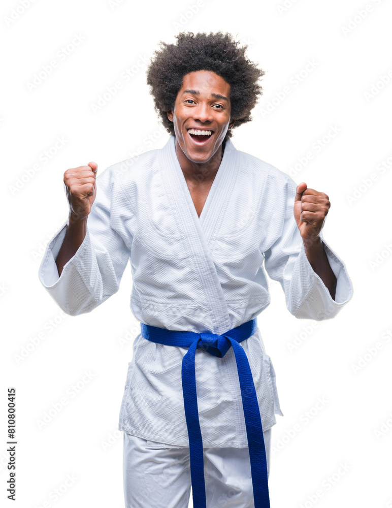 Afro american man wearing karate kimono over isolated background celebrating surprised and amazed for success with arms raised and open eyes. Winner concept. Afro american man wearing karate kimono over isolated background celebrating surprised and amazed for success with arms raised and open eyes. Winner concept.