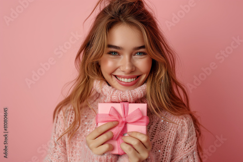 Woman with a gift.A girl in a hat and winter sweater on a bright background with a gift. New Year holidays concept. Christmas weekend and holidays. Boxing Day. photo