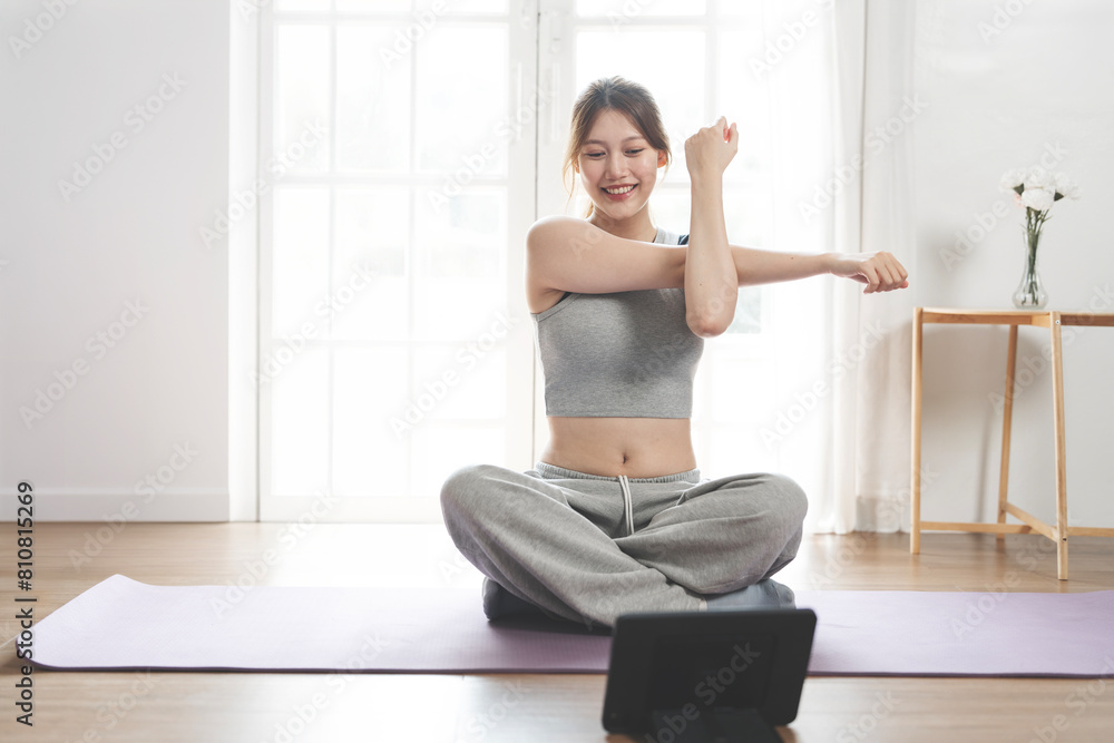 Cheerful active woman doing fitness at home,  sitting on the floor and watching online lessons on digital tablet