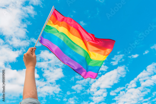 Hand waving rainbow LGBTQIA pride flag on sky background