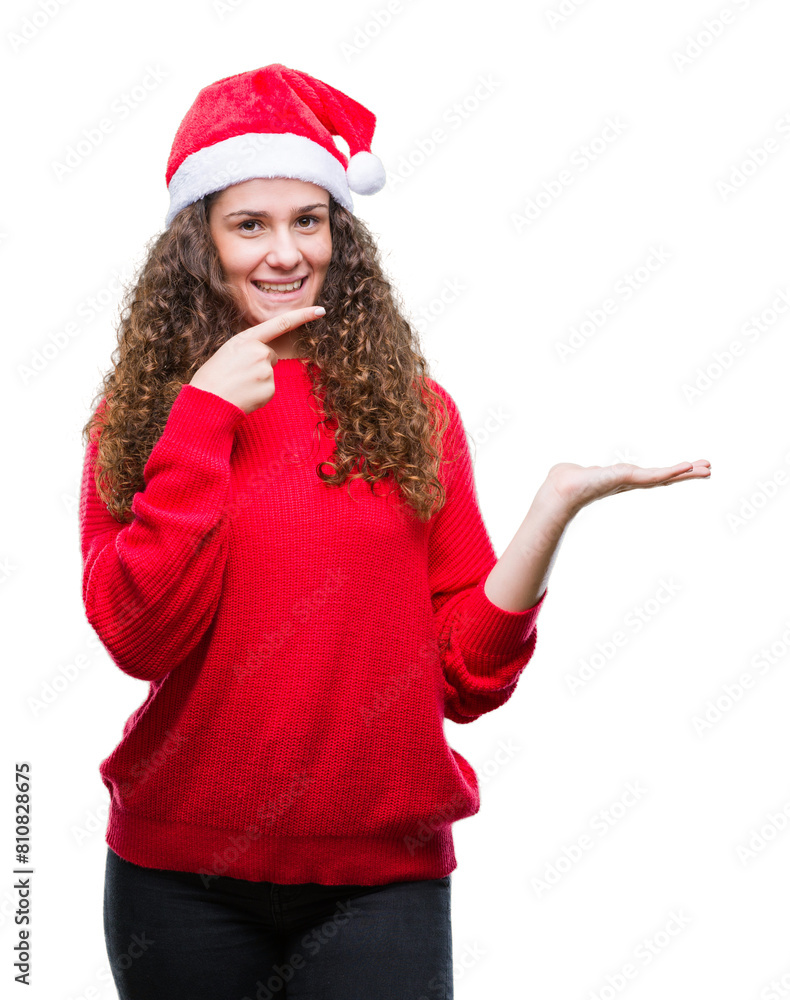 Young brunette girl wearing christmas hat over isolated background amazed and smiling to the camera while presenting with hand and pointing with finger. Young brunette girl wearing christmas hat over isolated background amazed and smiling to the camera while presenting with hand and pointing with finger.