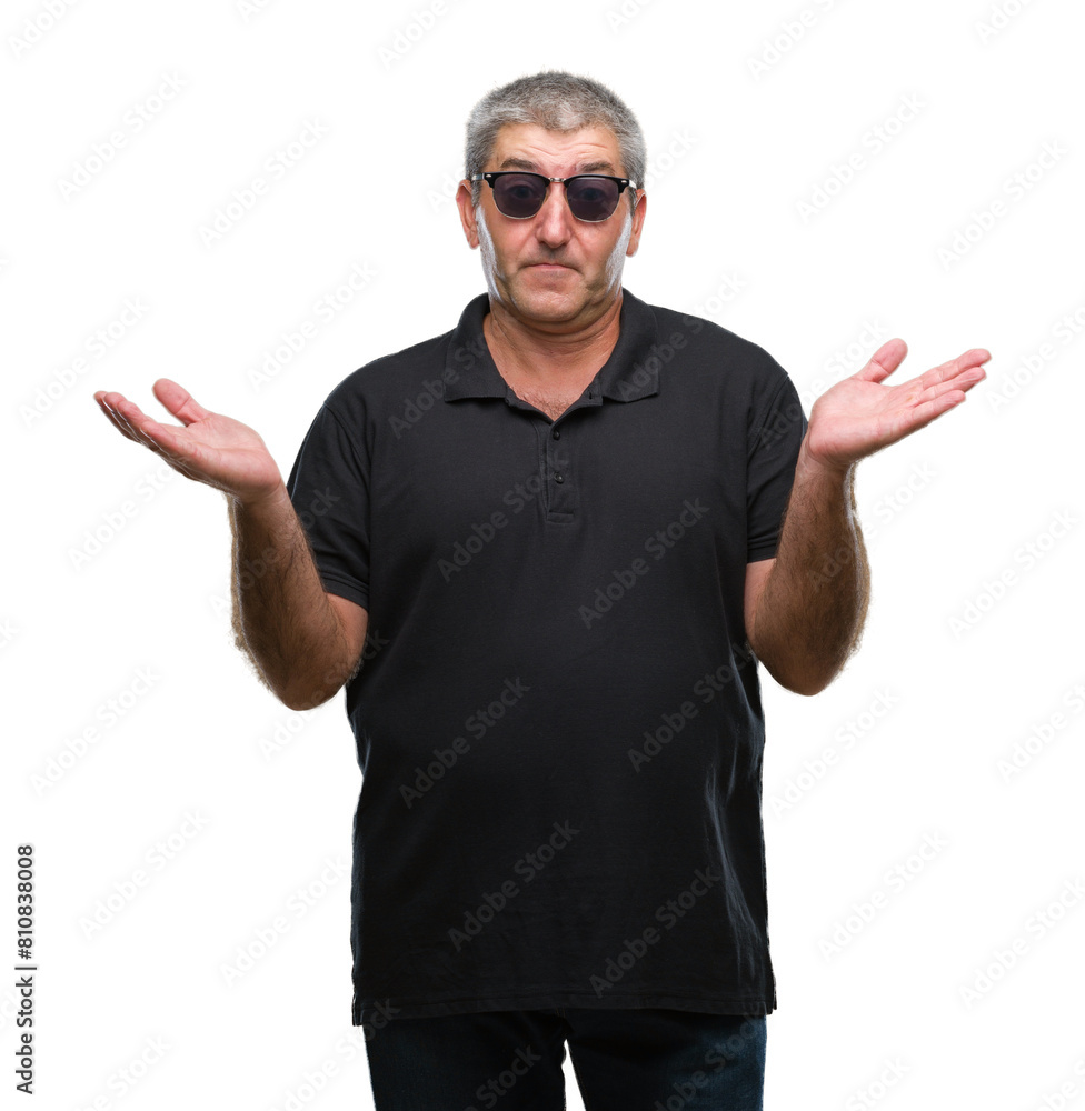 Naklejka premium Handsome senior man wearing sunglasses over isolated background clueless and confused expression with arms and hands raised. Doubt concept.