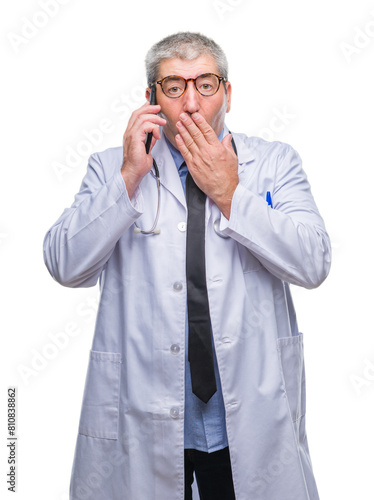 Handsome senior doctor man talking on smarpthone over isolated background cover mouth with hand shocked with shame for mistake, expression of fear, scared in silence, secret concept © Krakenimages.com