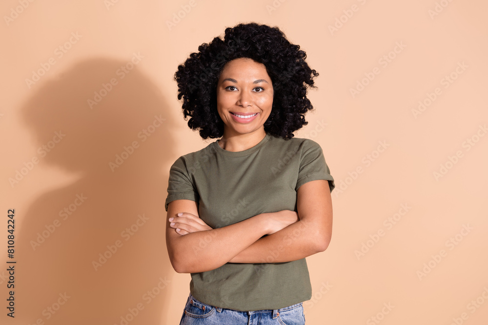 Portrait of good mood optimistic girl with afro hairdo dressed stylish t-shirt holding arms crossed isolated on beige color background Portrait of good mood optimistic girl with afro hairdo dressed stylish t-shirt holding arms crossed isolated on beige color background