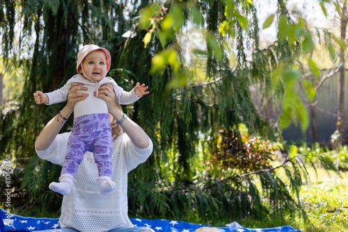 mother lifts baby in her arms, baby excitement, they spend time outdoors in the garden, sun, heat and shadow