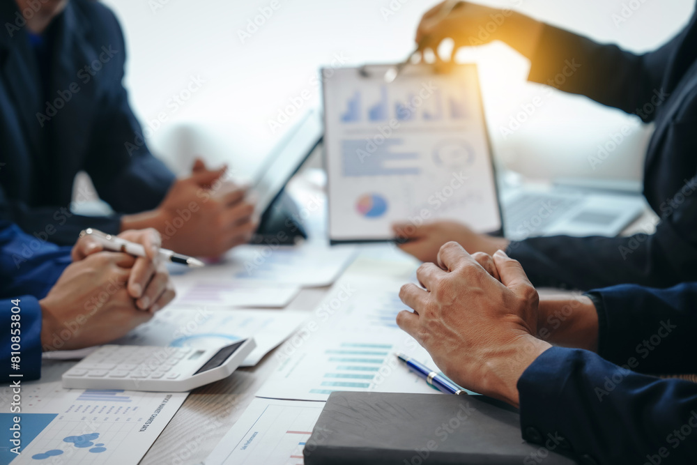 A professional business team meeting in formal suits, working at desks with financial papers, calculators, and laptops. Close-up of hands. Discussion on revenue, brand, sales, agenda, capital A professional business team meeting in formal suits, working at desks with financial papers, calculators, and laptops. Close-up of hands. Discussion on revenue, brand, sales, agenda, capital