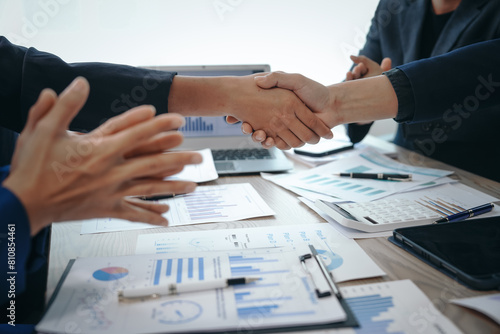 Fototapeta Naklejka Na Ścianę i Meble -  In a business team meeting, success is celebrated with a handshake. Hands close up, dressed in formal suits, working at desks with financial papers, calculators, and laptops.