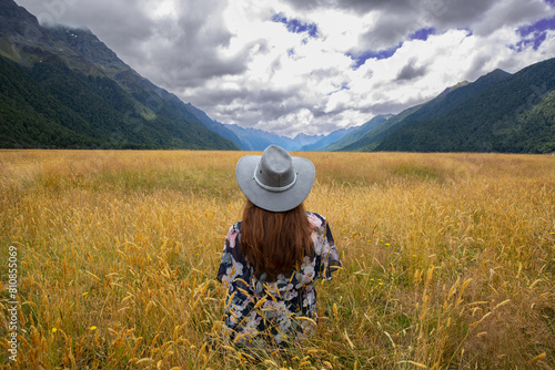 Open plains and wild grasses looking accross to Milford Sound, model wears a grey cowboy hat looking away from camera into distance