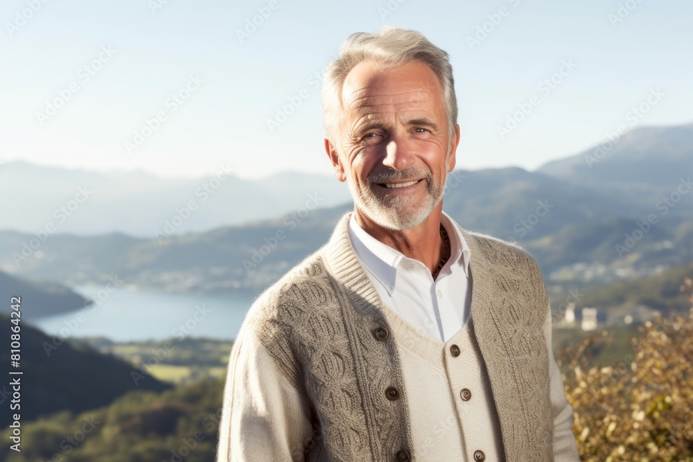 Portrait of a grinning man in his 60s wearing a chic cardigan in panoramic mountain vista Portrait of a grinning man in his 60s wearing a chic cardigan in panoramic mountain vista