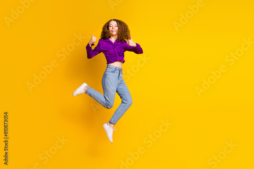 Full length photo of lovely young lady jump running show thumb up dressed stylish violet garment isolated on yellow color background