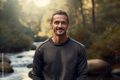 Portrait of a satisfied man in his 40s dressed in a comfy fleece pullover in front of tranquil forest stream
