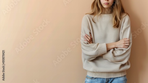 young woman in beige sweater and jeans standing with arms crossed against light brown background, copy space, rejection concept
