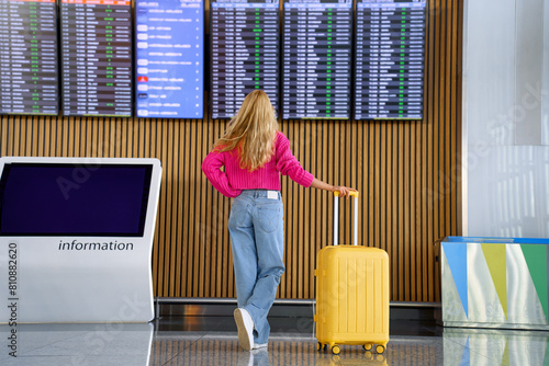 woman with luggage looks at airplane schedule board at airport