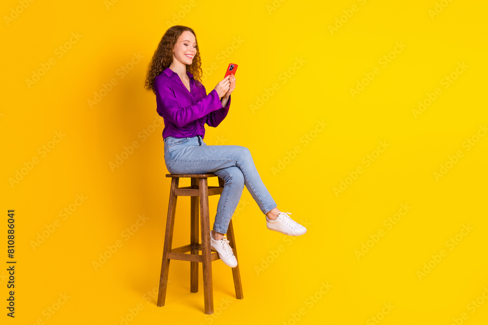 Full body photo of pretty young girl sit chair hold device wear trendy violet outfit isolated on yellow color background Full body photo of pretty young girl sit chair hold device wear trendy violet outfit isolated on yellow color background