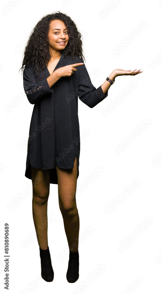 Young beautiful girl with curly hair wearing elegant dress amazed and smiling to the camera while presenting with hand and pointing with finger. Young beautiful girl with curly hair wearing elegant dress amazed and smiling to the camera while presenting with hand and pointing with finger.