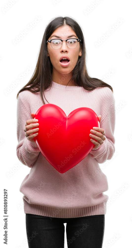 Young hispanic woman holding heart in love scared in shock with a surprise face, afraid and excited with fear expression Young hispanic woman holding heart in love scared in shock with a surprise face, afraid and excited with fear expression