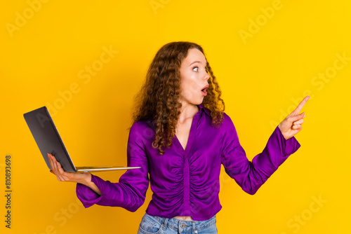 Photo portrait of pretty young girl hold laptop point look scared empty space wear trendy violet outfit isolated on yellow color background photo